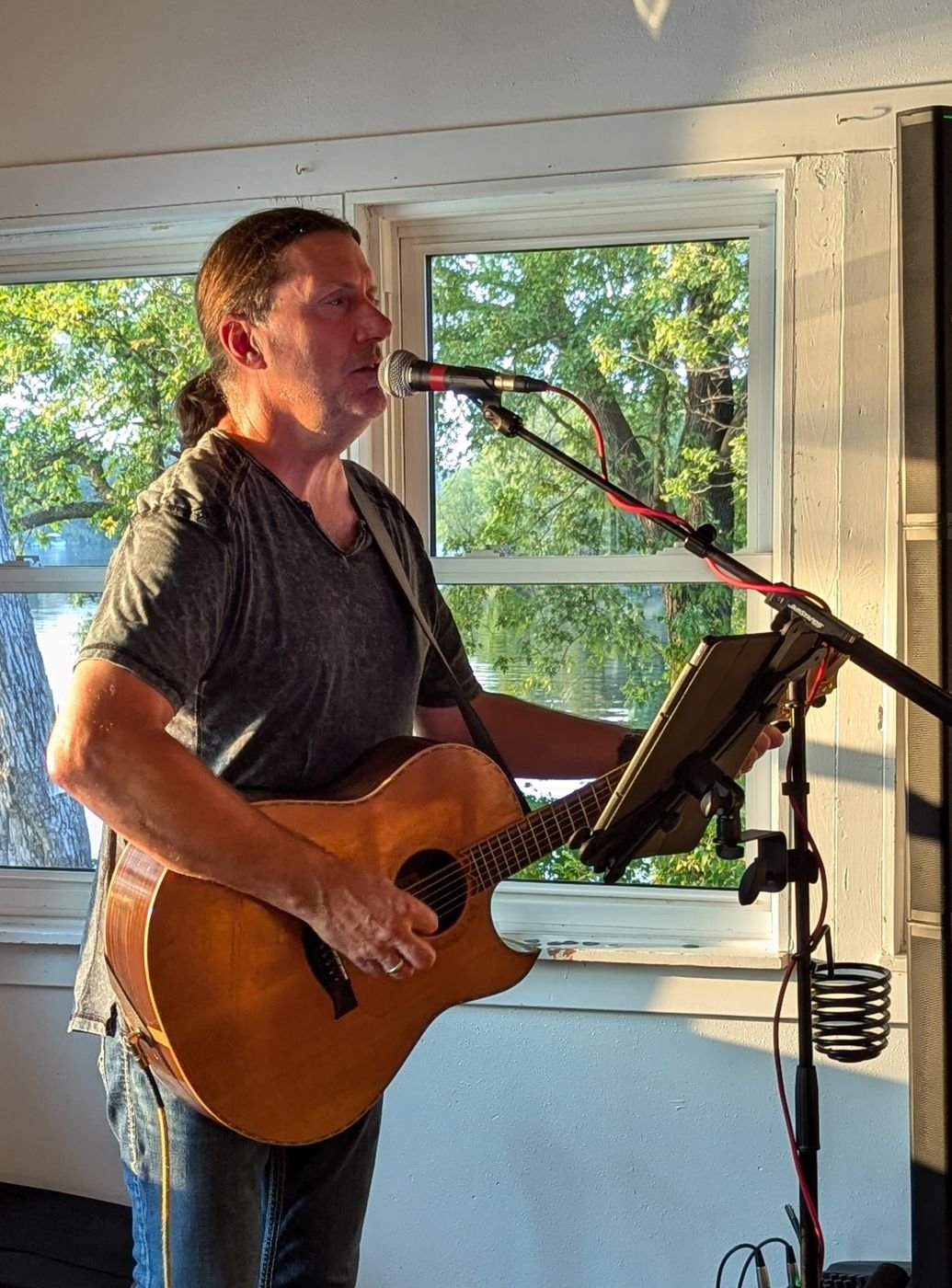 Denny Menter performing acoustic guitar by a window at sunset