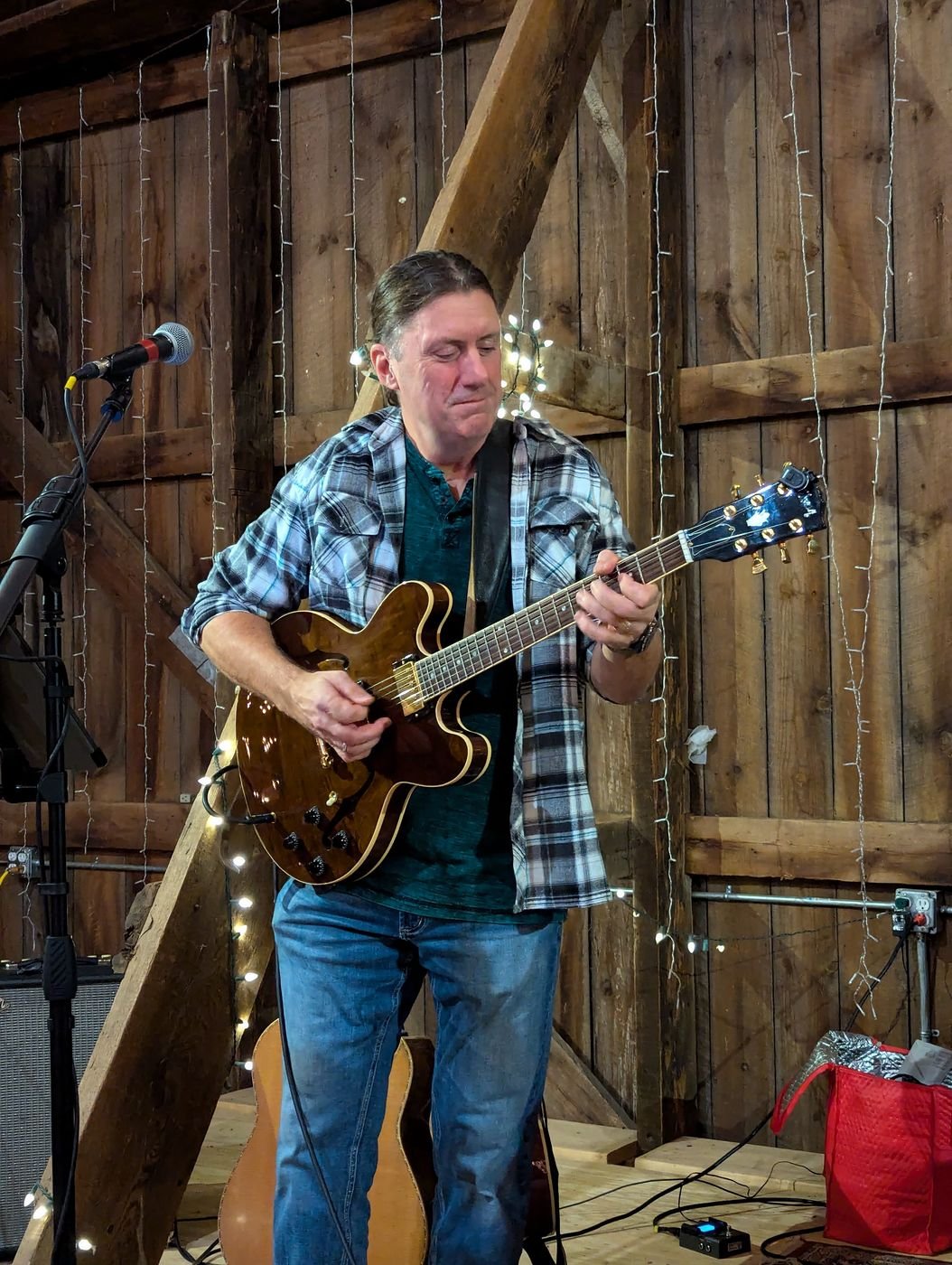 Denny Menter playing electric guitar in a barn venue strung with lights